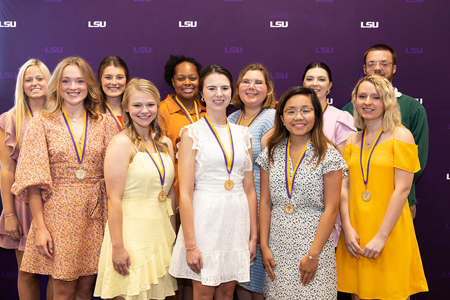 group of eleven students pose in front of purple backdrop