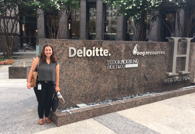 A female CIA&CRM student stands outdoors in front of a sign indicating an office of Deloitte, where she is interning. 